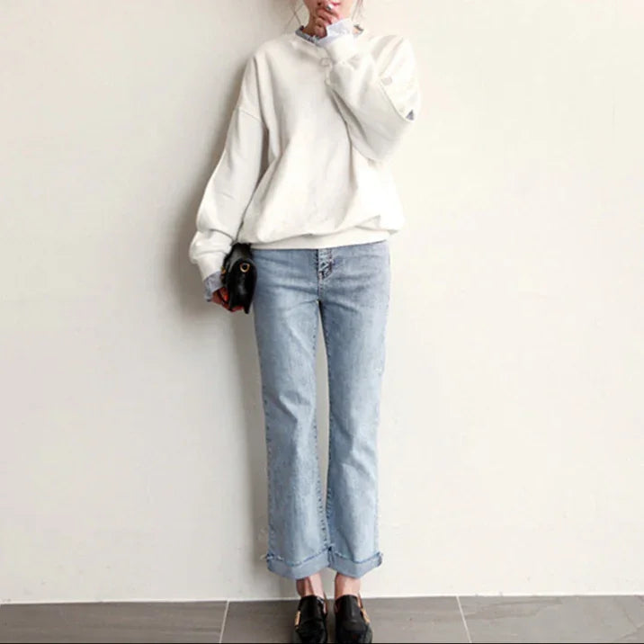 Person wearing a white sweatshirt and light blue jeans against a plain background