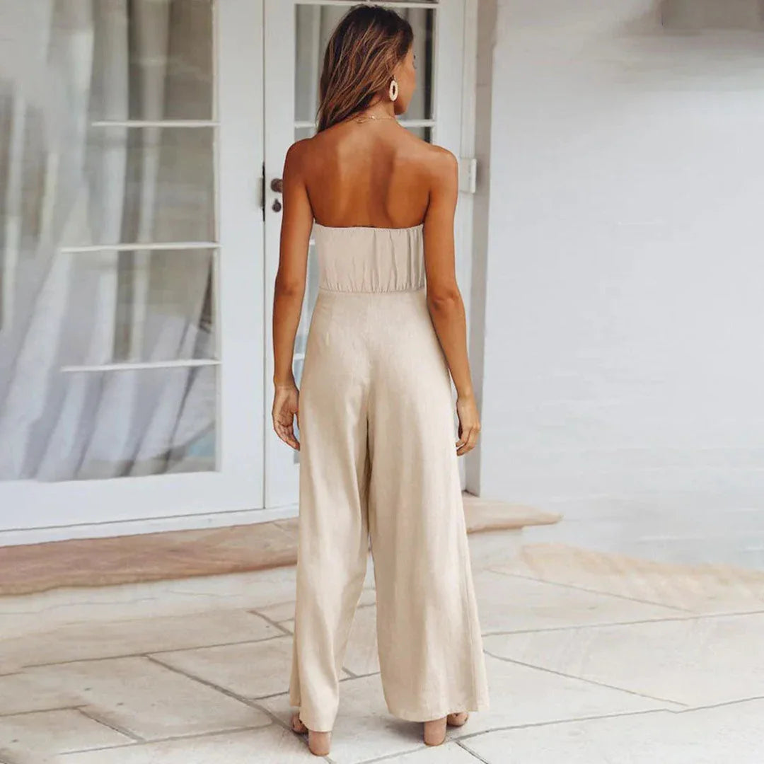 Woman wearing a beige strapless jumpsuit standing in a bright room with large windows.