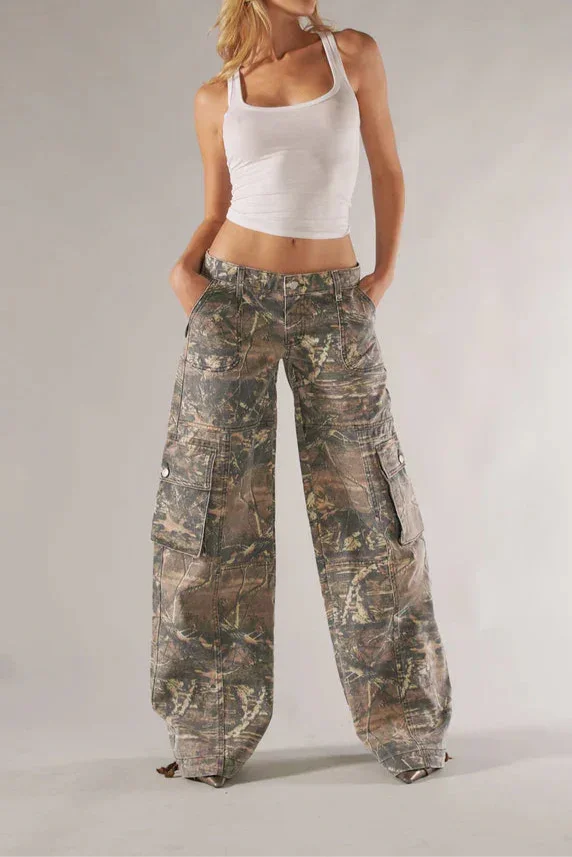 Woman wearing a white tank top and camouflage pants on a plain background