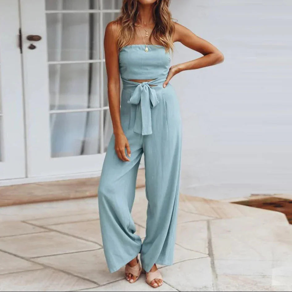 Woman wearing a light blue strapless top and wide-leg pants standing on a patio.