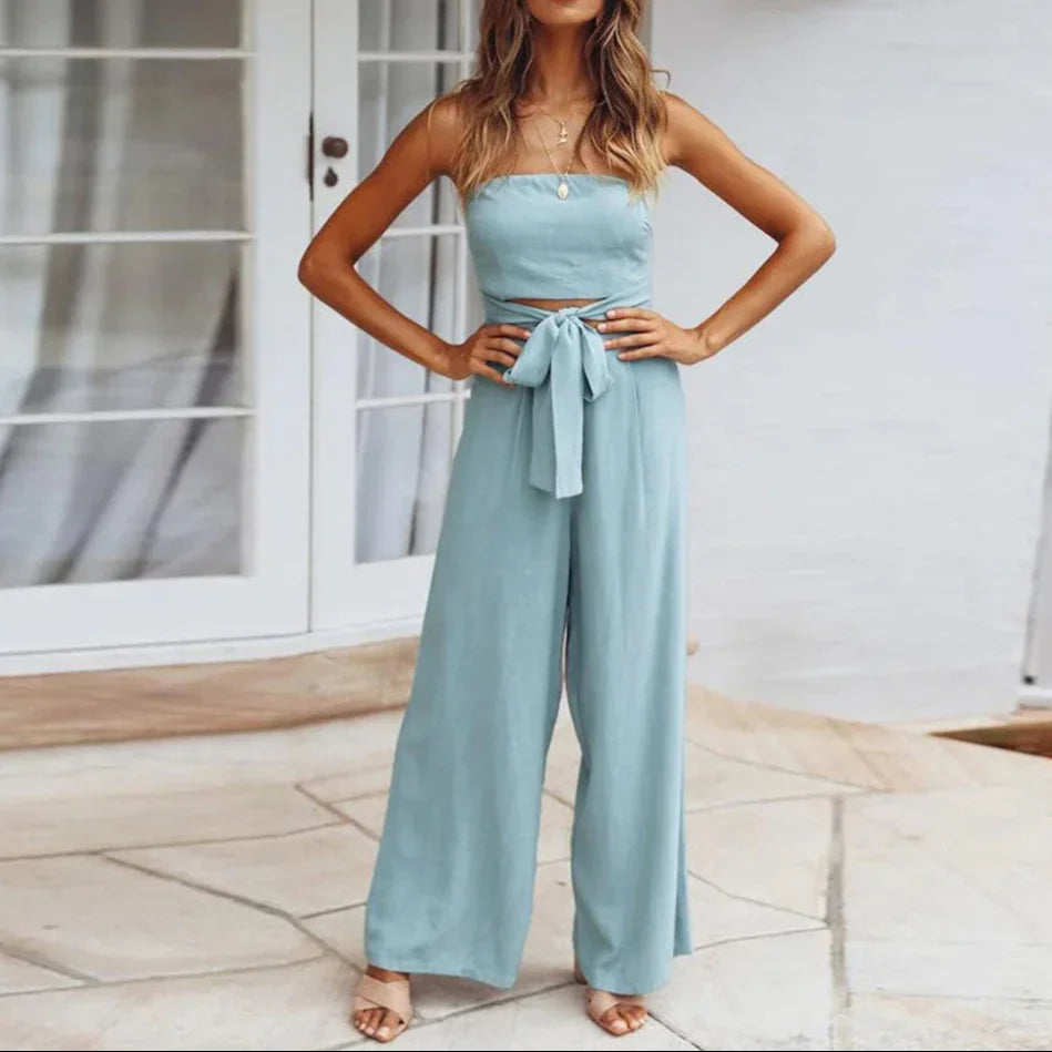 Woman wearing a light blue outfit with wide-leg pants and a top, standing on a patio.
