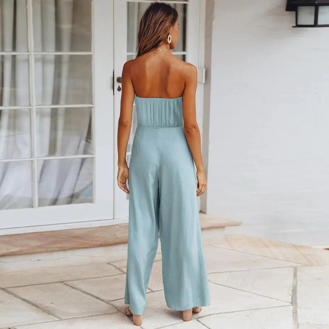 Woman wearing a light blue strapless jumpsuit standing in a sunlit room.