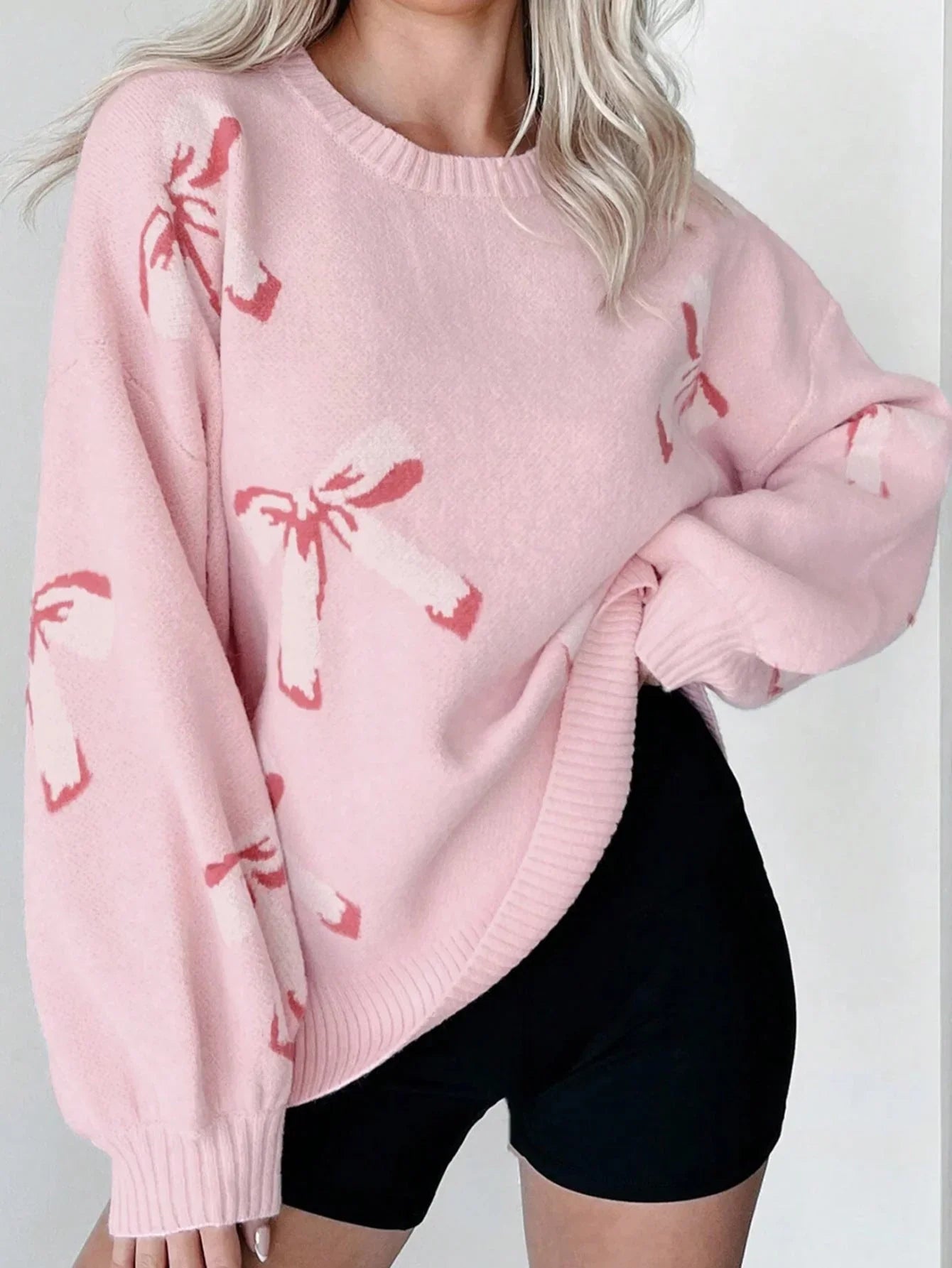 Person wearing a pink sweater with red patterns on a plain background