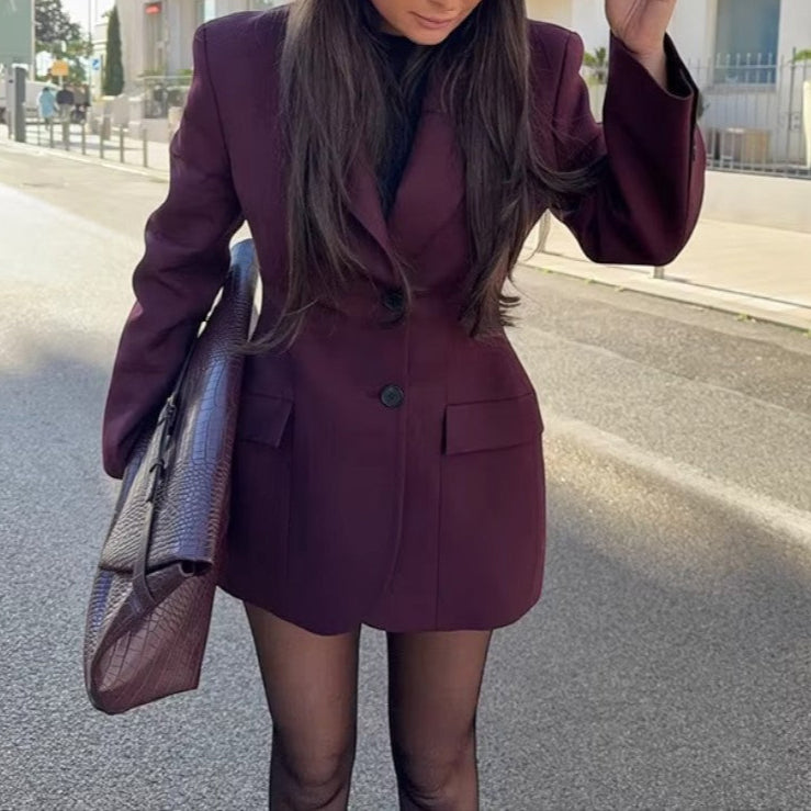 Woman in a burgundy suit and black hat standing on a street with buildings in the background
