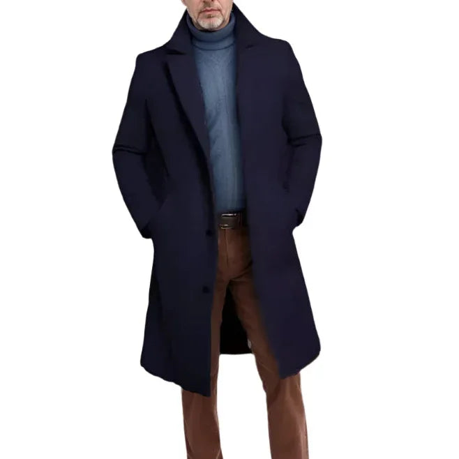Man wearing a navy coat over a blue sweater and brown pants on a white background