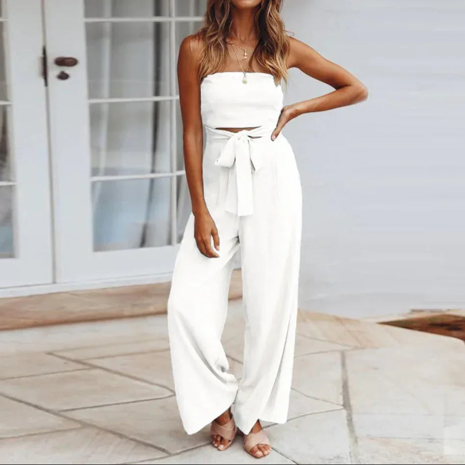 Woman wearing a white strapless top and wide-leg pants standing on a patio.