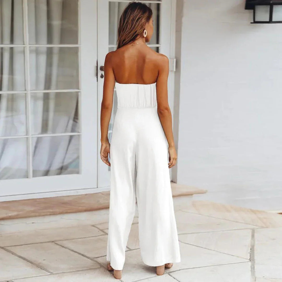 Woman wearing a white strapless jumpsuit standing in a bright outdoor setting.