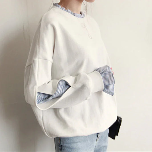 Person wearing a white sweater with striped cuffs and hem against a plain background