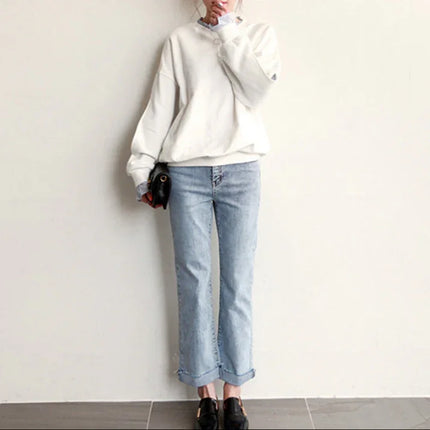 Person wearing a white sweatshirt and light blue jeans against a plain background