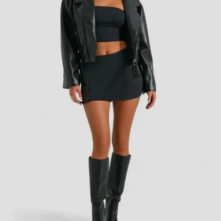 Woman wearing a black leather jacket, top, skirt, and boots on a light gray background