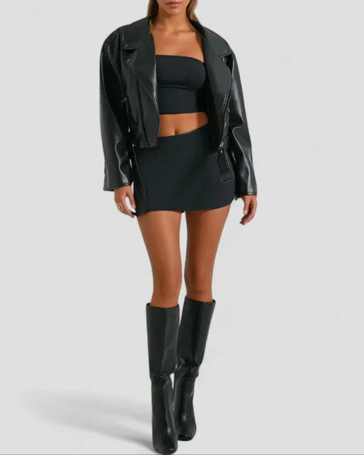 Woman wearing a black leather jacket, top, skirt, and boots on a light gray background