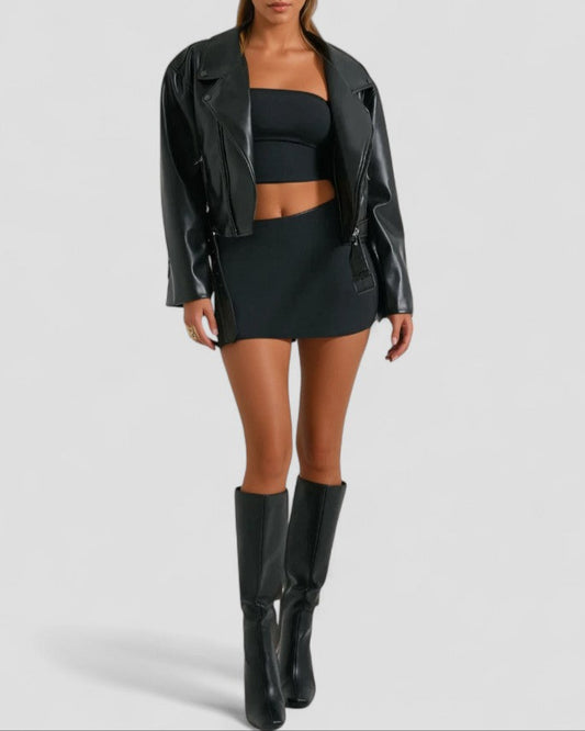 Woman wearing a black leather jacket, top, skirt, and boots on a light gray background