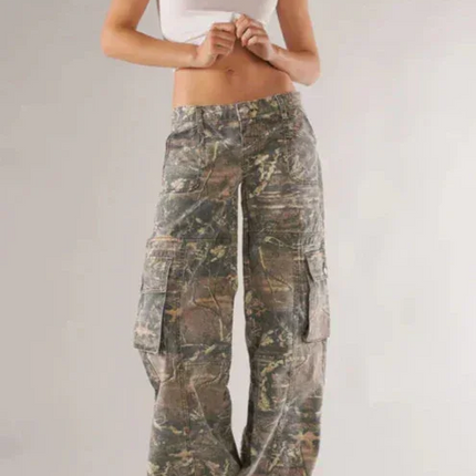 Woman wearing camouflage pants and a white top on a plain background