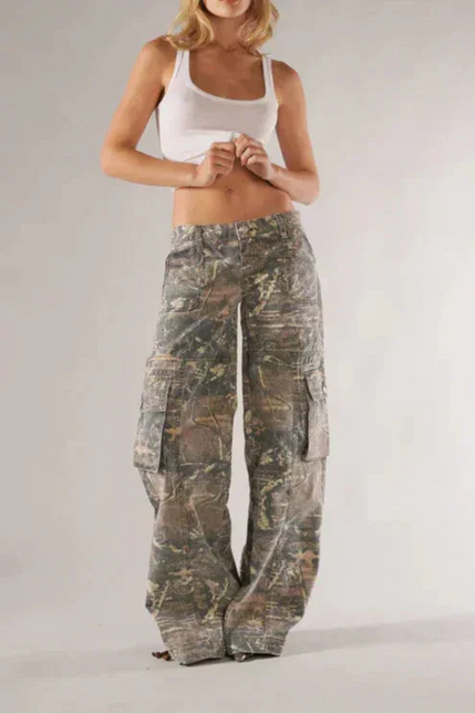 Woman wearing camouflage pants and a white top on a plain background