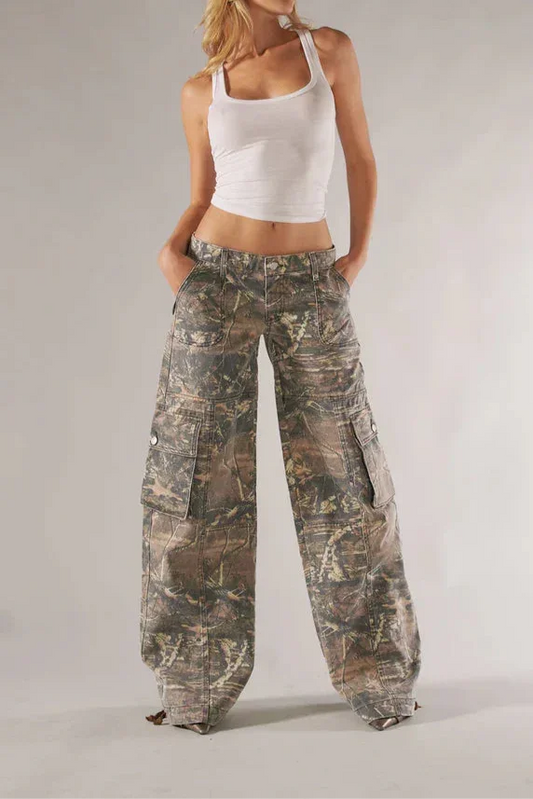 Woman wearing a white tank top and camouflage pants on a plain background