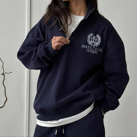 Woman wearing a navy blue tracksuit with a logo against a gray background