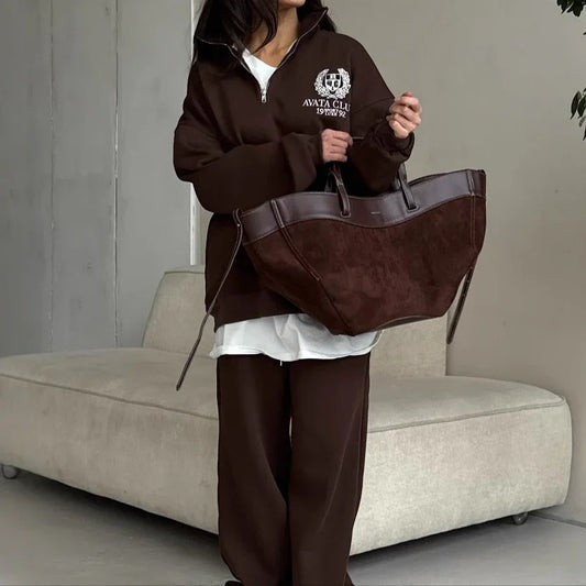 Person wearing a brown hoodie and holding a matching bag in an indoor setting.
