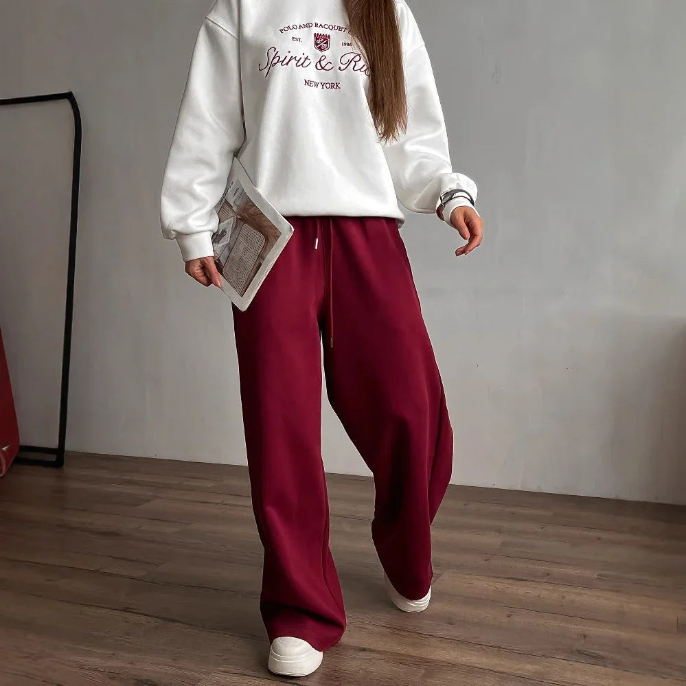 Person wearing a white sweatshirt and red pants holding a magazine indoors.