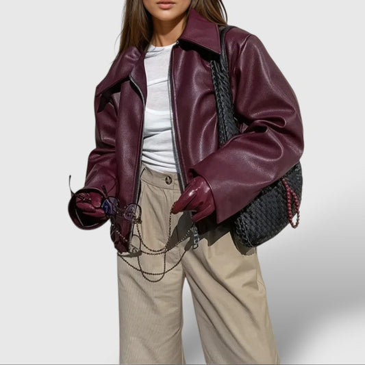 Woman wearing a burgundy leather jacket with a white shirt and beige pants on a light gray background