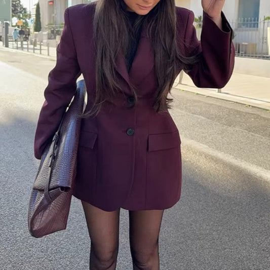Woman in a burgundy suit and black hat standing on a street with buildings in the background