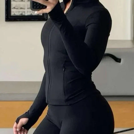 Woman in black athletic wear taking a mirror selfie in a room with framed pictures on the wall.