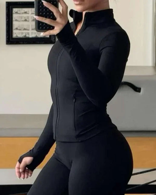 Woman in black athletic wear taking a mirror selfie in a room with framed pictures on the wall.