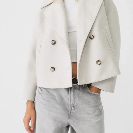 Woman wearing a light gray jacket over a white top and denim shorts on a white background