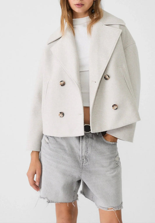 Woman wearing a light gray jacket over a white top and denim shorts on a white background